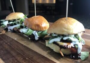 Three sandwiches are lined up on a wooden board.